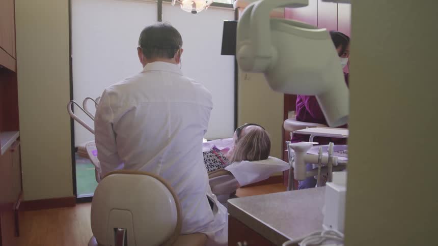 A female patient is reclined in an an examination chair in a dental office as the dentist prepares to look in her mouth