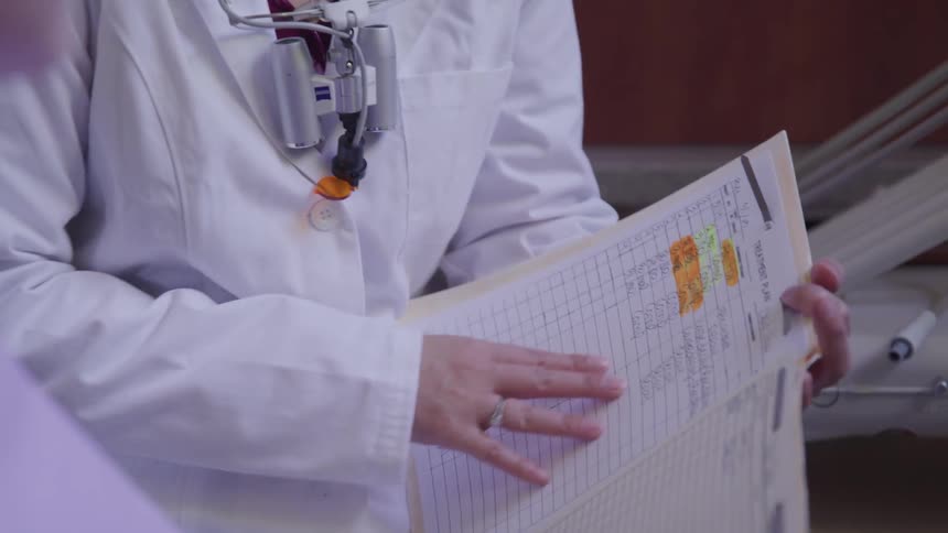A medical professional talks with another person while holding a medical file