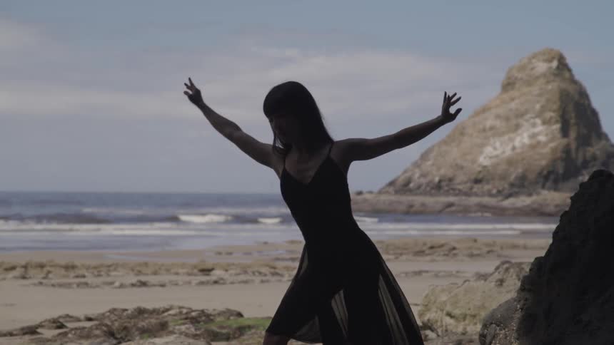 A woman in a black shawl dancing on the beach