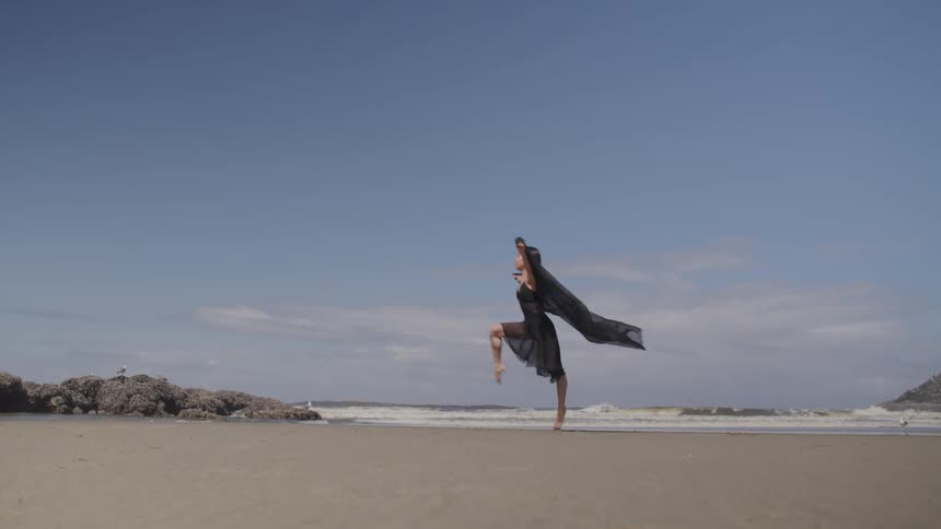 A woman in a black shawl dancing on the beach