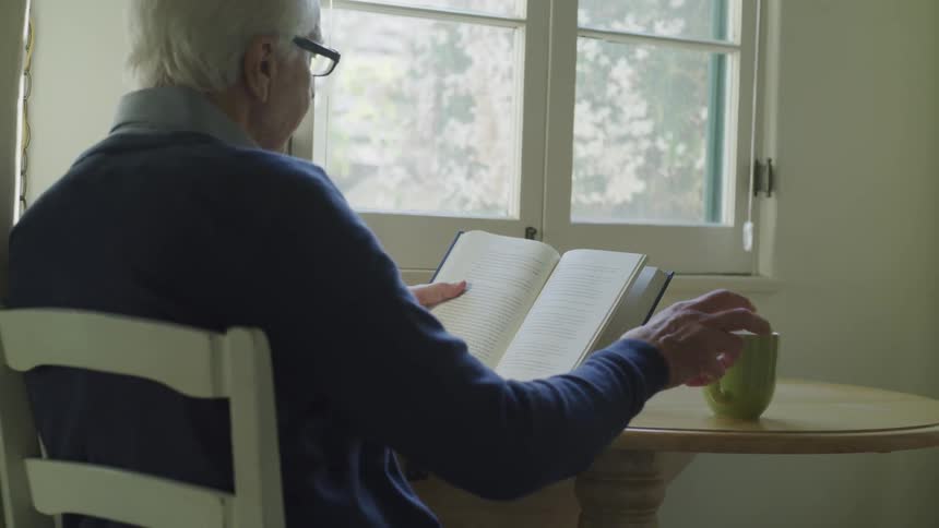 An old man reading a book with a cup of coffee