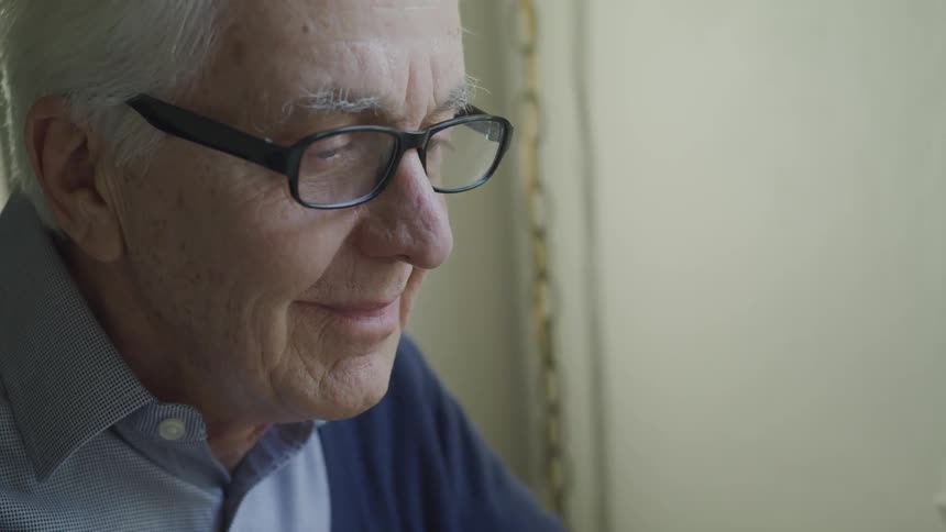 An old man with glasses sits and smiles widely