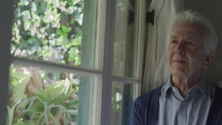 Old man looks out the window in the bedroom