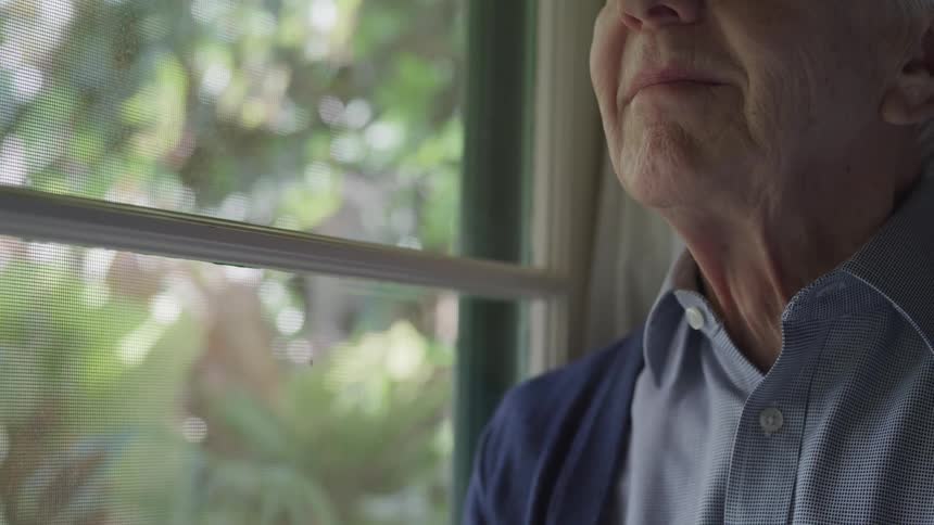 An elderly man stands beside a window