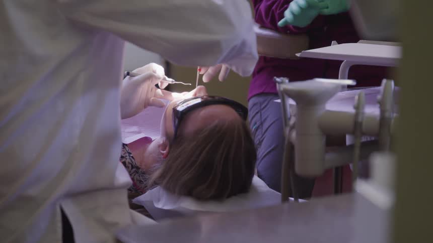 Dentist treating patient in office assisted by nurse