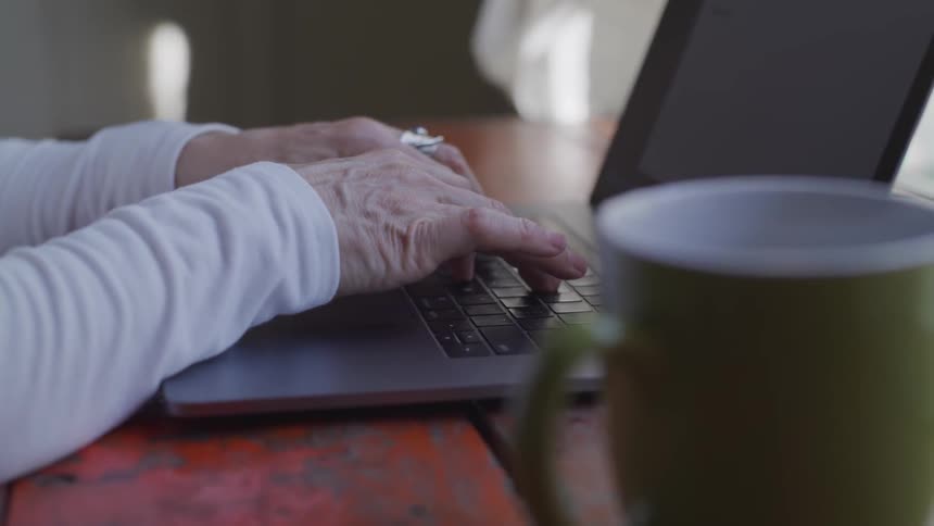 An elderly woman types on a laptop