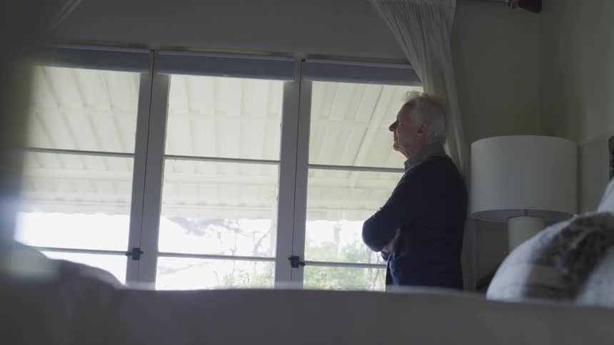 A man is standing in his bedroom looking out the window