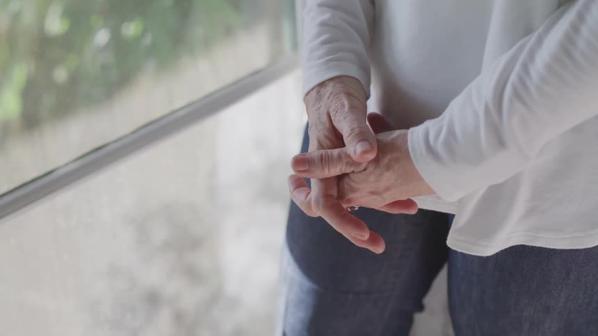 A person standing before a window clasping their hands together