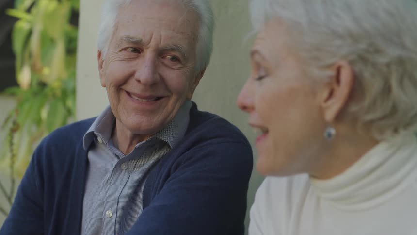 Older couple sit outside house talking