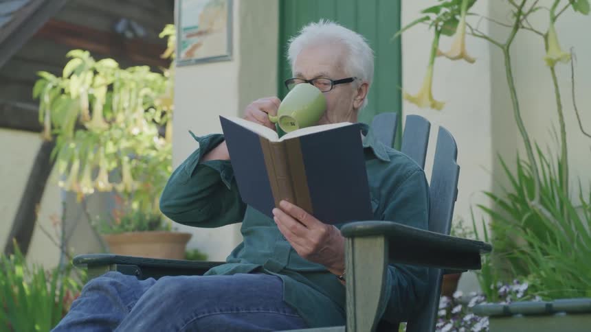 An older man drinking from a cup and reading outside