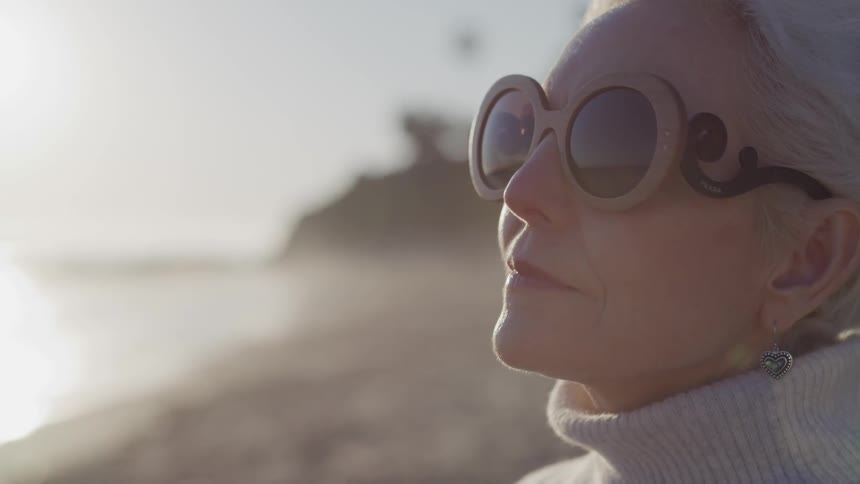 A woman wearing sunglasses sits on the beach