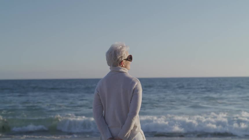 Elderly woman standing on the beach looking at the ocean