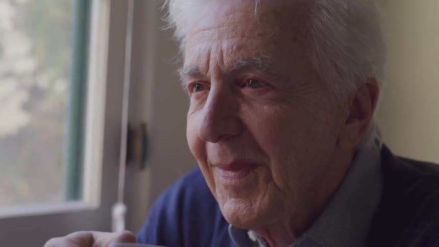 An elderly man sits and talks while drinking coffee