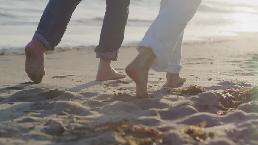 Man and woman walk barefoot along the white sand beach at sunset next to the ocean