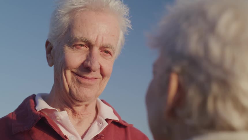 Old man and woman look and smile at each other on the beach at sunset