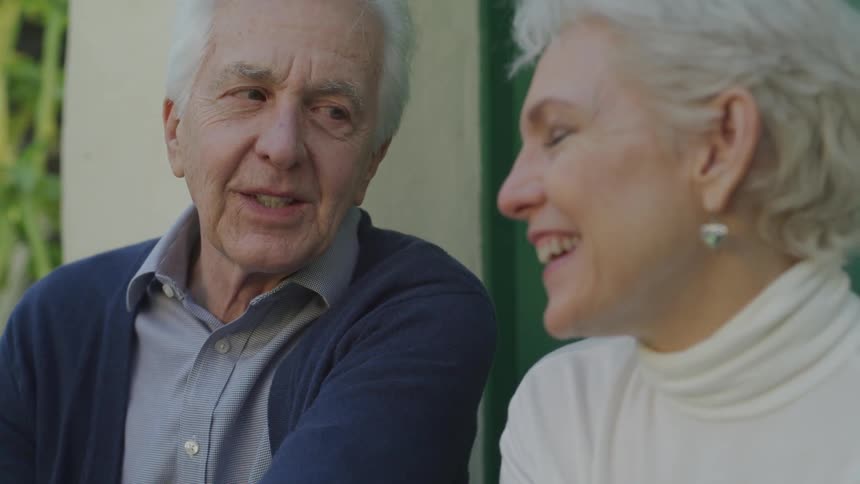 An elderly man and woman sit and talk
