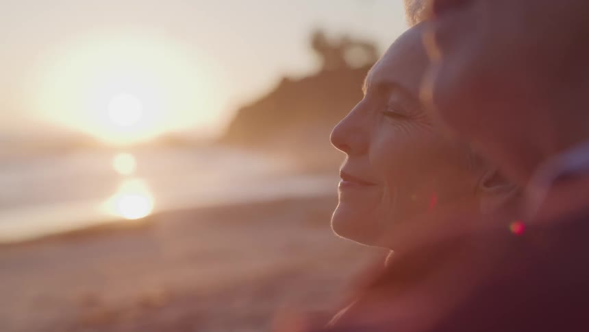 Man and woman sit together on the beach as the sun sets over the ocean