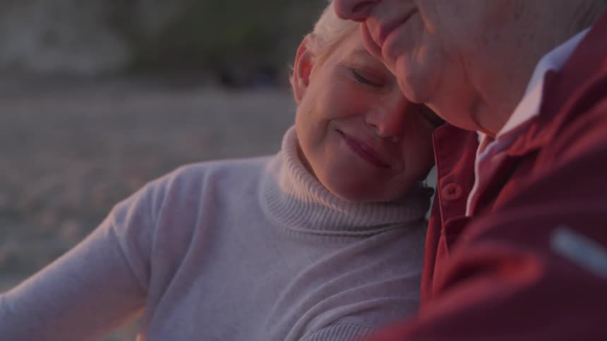 An elderly man and woman sit and cuddle together