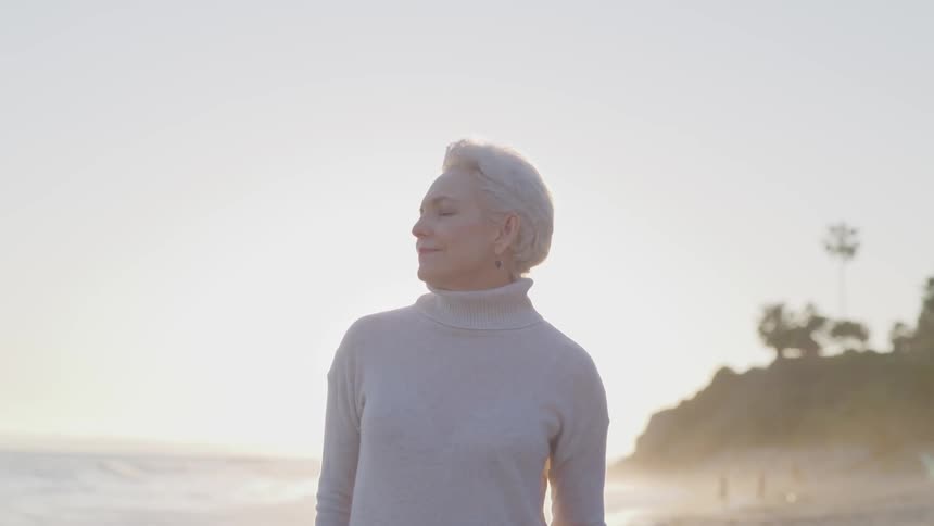A woman stands on the beach with her eyes closed
