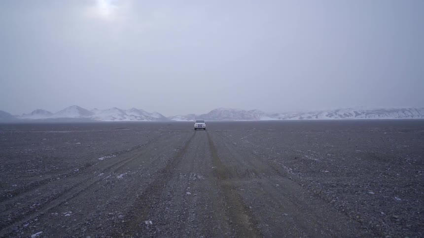 A vehicle drives near snow-covered mountains