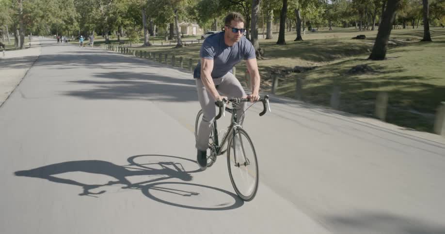 A man wearing sunglasses peddles a bike down the middle of a road
