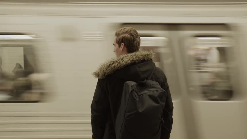 A young man stands on a platform as a train pulls up