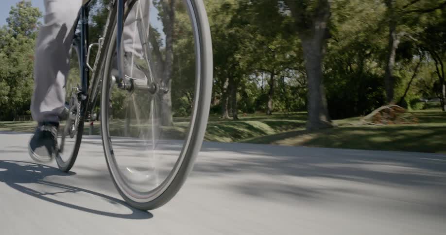 A man is riding a bike down a two lane road near a park on a sunny day