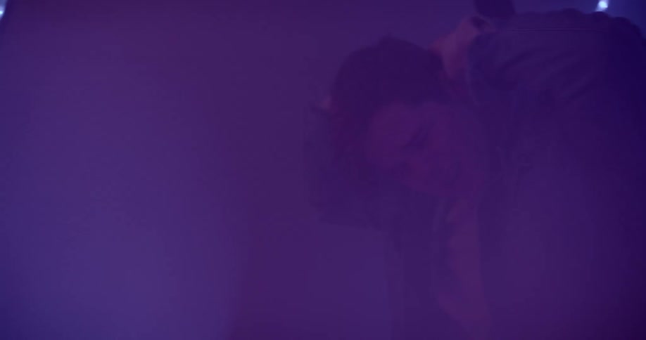 A young man raises his arms in a foggy and dimly lit room