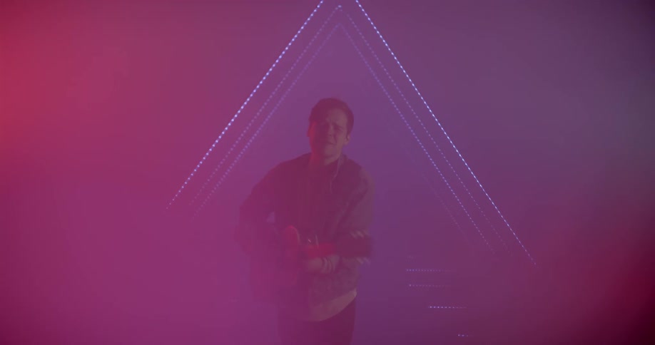 A man plays guitar in a studio environment with a blue triangle outline illuminating the background