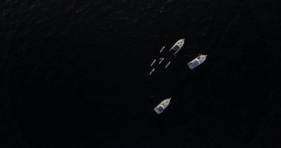 Five kayaks follow three larger boats on the open water
