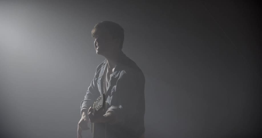 Male singer screams and plays a guitar in the spotlight in the dark music studio