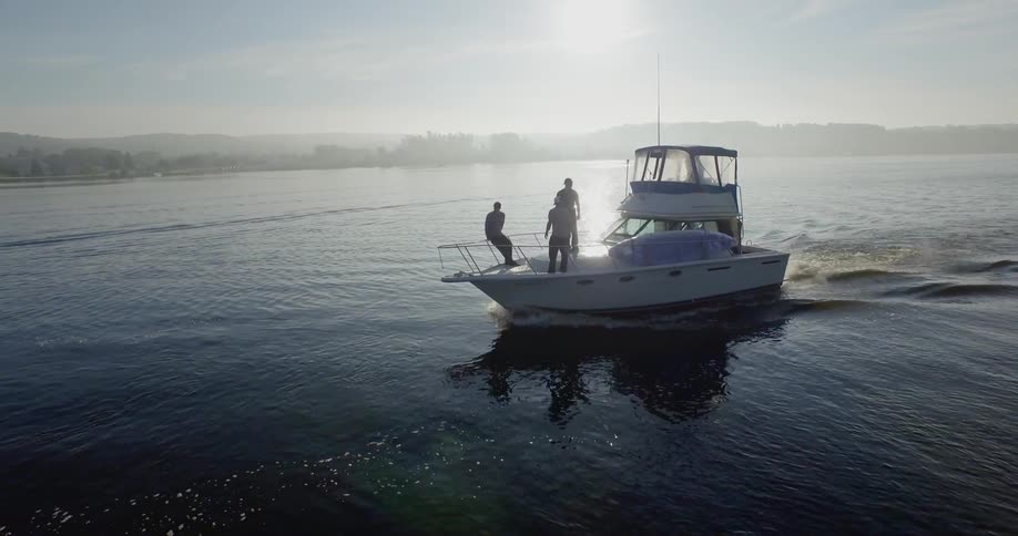 Three men are standing near the railings at the bow of a boat traveling across a calm lake