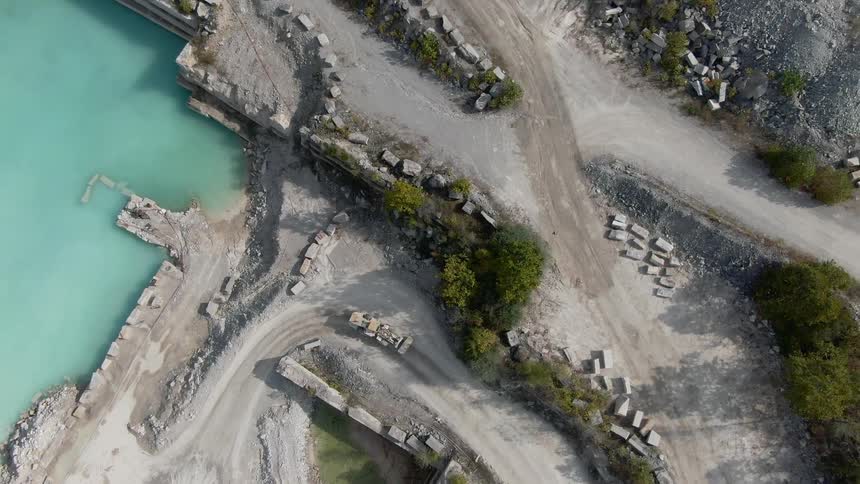 A bulldozer travels on a curving dirt road near water and gravel piles