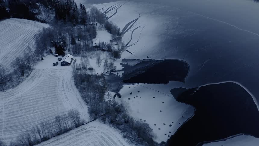 A frozen lake near snow covered fields and houses