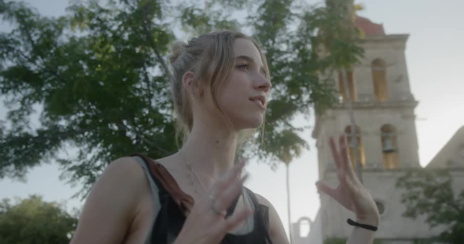 A young woman speaks with another person in front of a large church with a bell tower