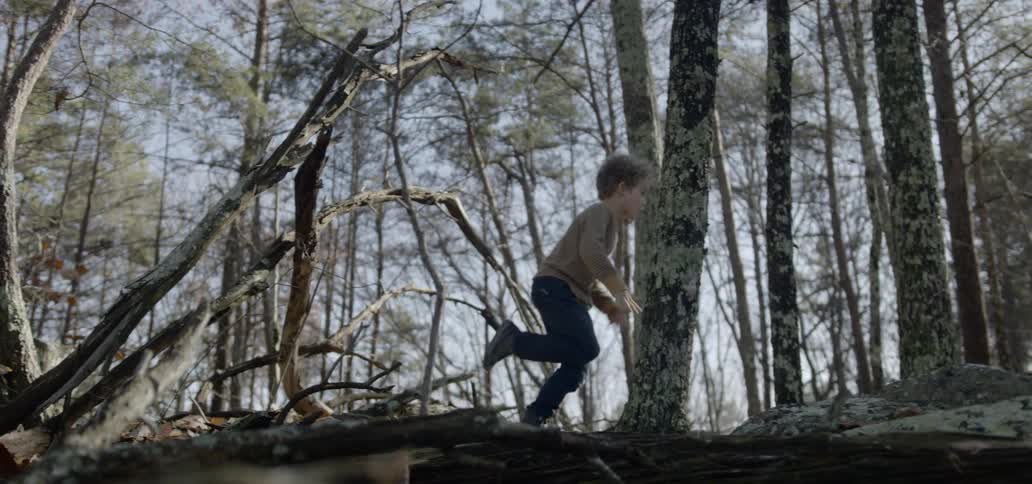 A boy ducking under branches walking through the woods