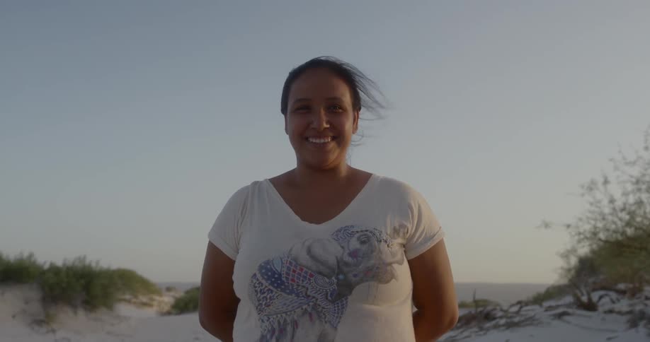 A woman standing at the beach on a windy day smiles directly at the camera