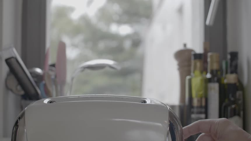 A person pops bread out of a toaster
