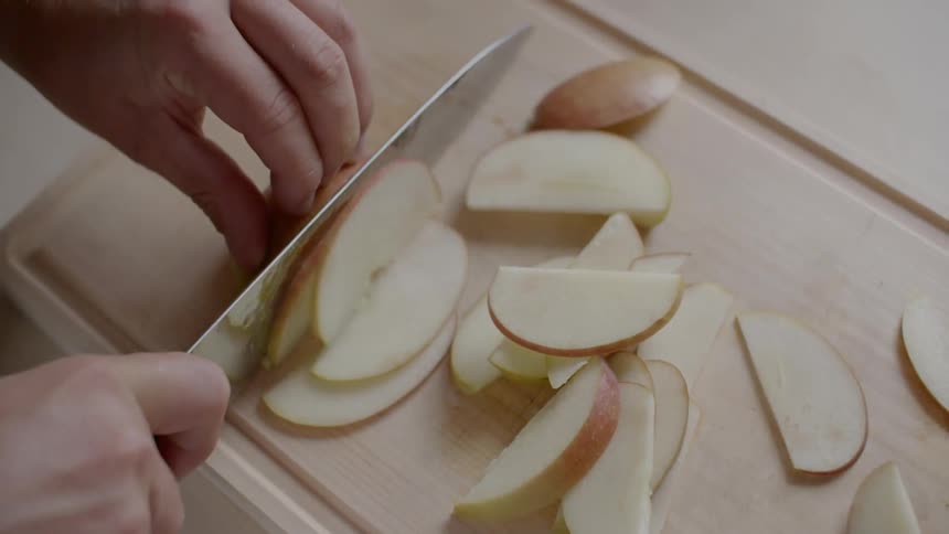 A person is using a large kitchen knife to cut an apple into thin slices
