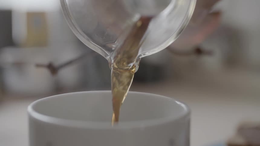 A person pours hot liquid out of a beaker and in to a mug