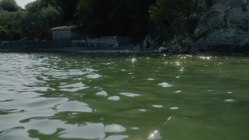 Sunlight sparkles off small waves near forested cliff side and shed