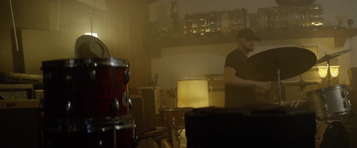A drummer plays in a lowly lit studio