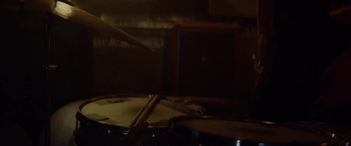 A person walks up to a drum set then sits down at it an picks up the drum sticks