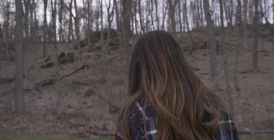 A woman stands alone in a forested area