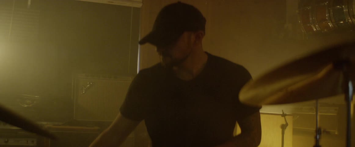 A drummer walks over to a drum kit in a softly lit studio