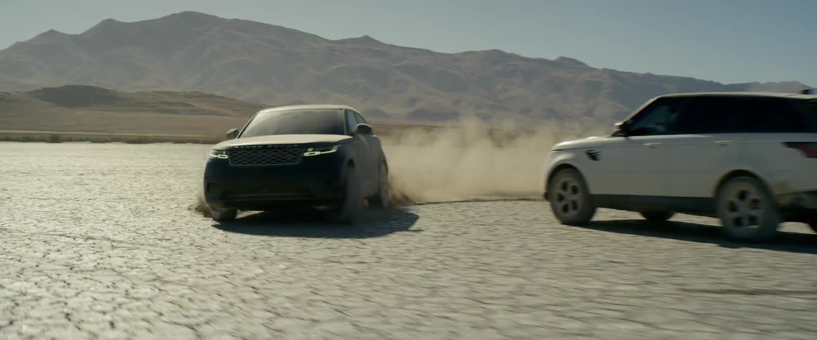 A black suv circles a white vehicle on the salt flats kicking up a dust cloud