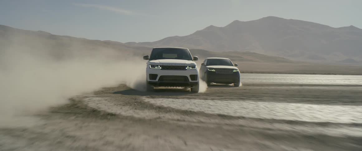 Two vehicles driving in the desert with a mountain and the sky in the background