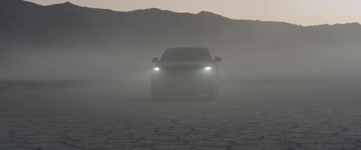 A car turns its headlights on in a foggy desert at dusk