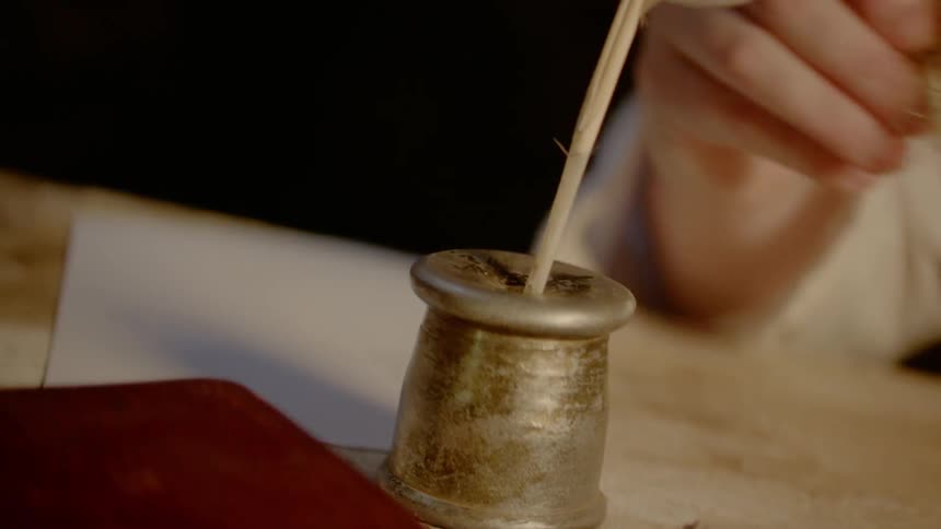 A person dipping a quill in an inkwell