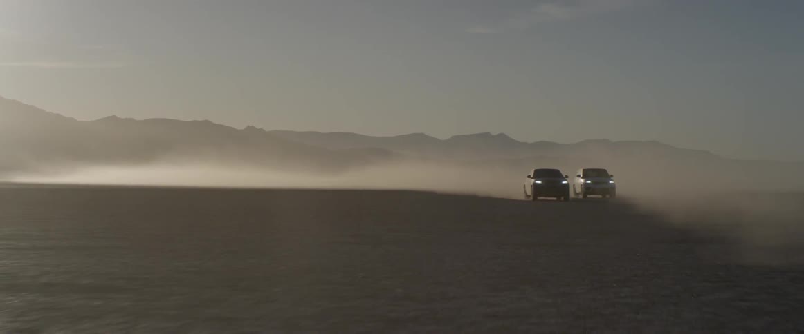 Two range rover sports race on the salt flats kicking at sunset